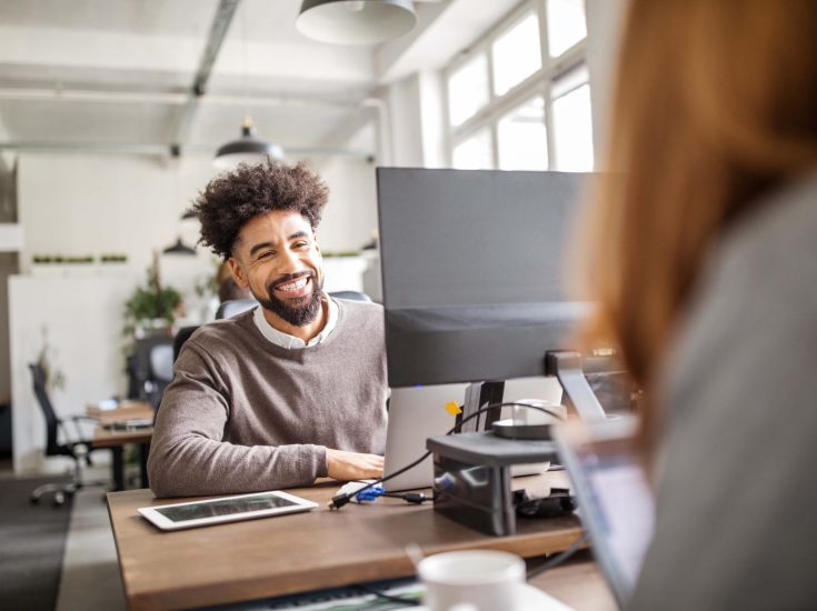 Smiling african businessman talking with female colleague while working at his desk. Young business professionals working in office.